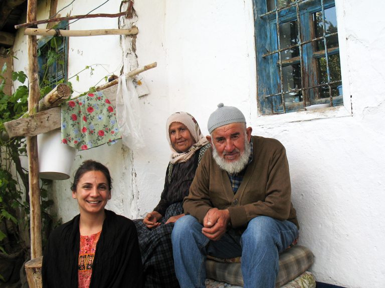 Three people sitting on a bench in front of a house.
