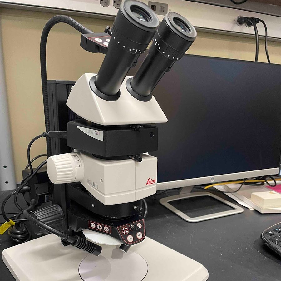 Leica microscope on a lab bench with a computer monitor in the background.