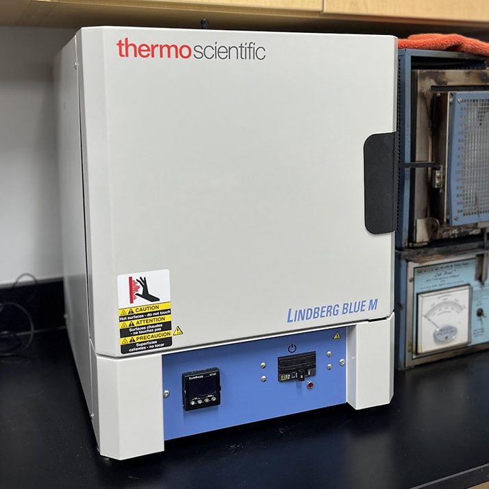 A thermo scientific lindberg/blue m lab oven on a bench, surrounded by other laboratory equipment.