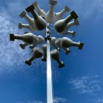 A cluster of white, dome-shaped objects attached to a tall metal pole, set against a blue sky with scattered clouds.