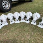 Eight white helmet-like devices labeled A to H are arranged on the grass in front of a vehicle.