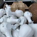 A truck bed filled with white, conical-shaped objects, several cardboard boxes, and a large bundle of dried twigs.