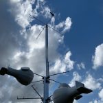 A tall pole with antennas and large bulbous attachments stands against a partly cloudy sky.