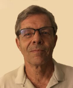 A middle-aged man with gray hair, glasses, and a mustache, wearing a light-colored collared shirt, against a plain background.