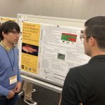 Two people stand in front of a scientific poster titled "Ecological and Genetic Divergence by Color Morph in the Red Eye Hawkfish Paracirrhites Arcatus," discussing its content.