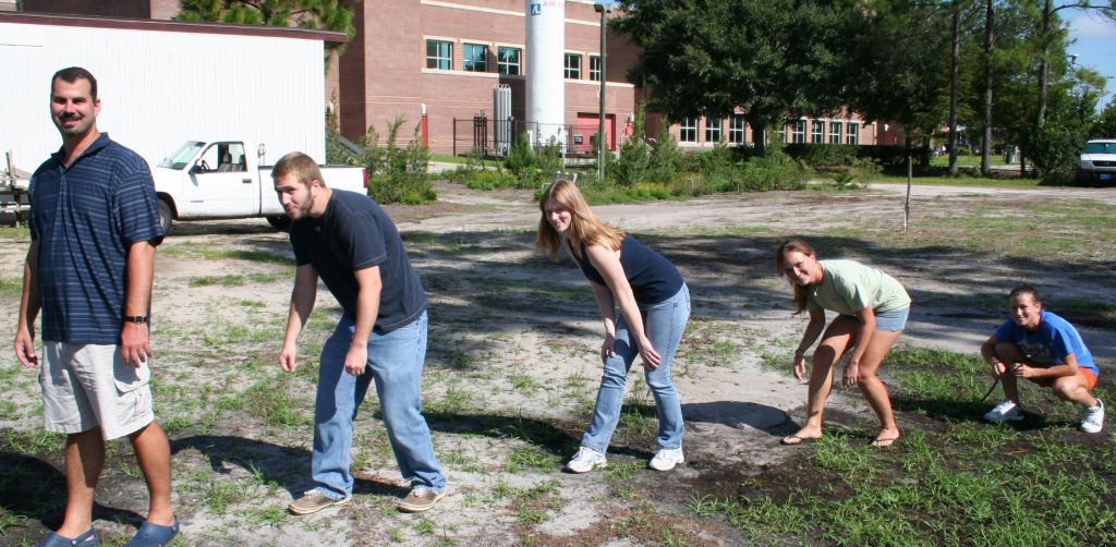 Five people outdoors mimicking the evolution of humans, starting crouched and ending upright.