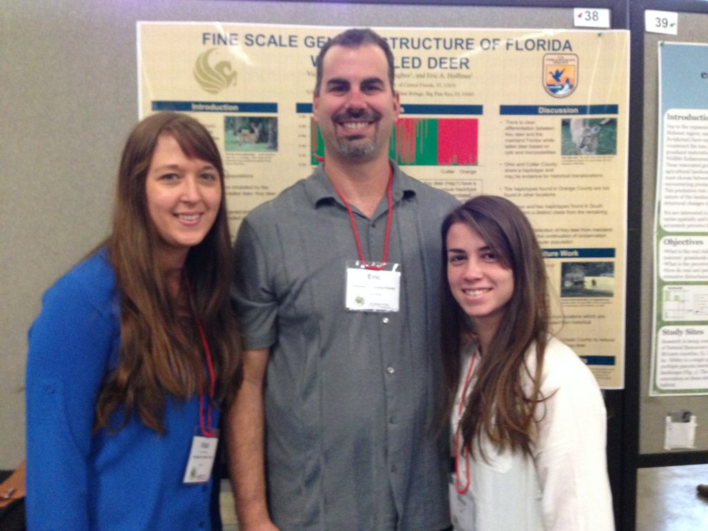 Three people stand in front of a research poster about Florida Key Deer.