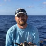 Person holding a small sea turtle on a boat with the ocean in the background.