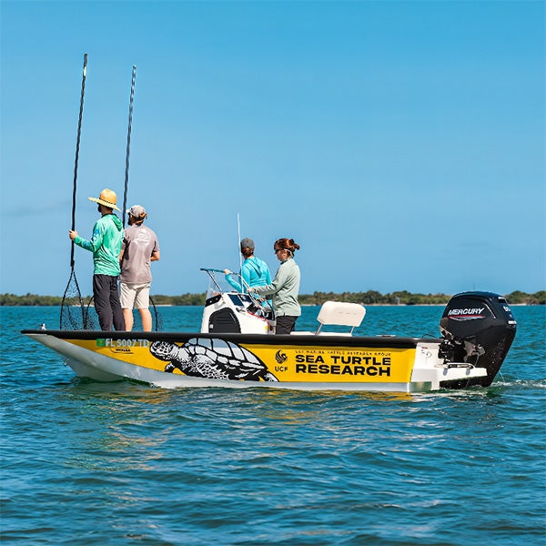 A small boat labeled "Sea Turtle Research" with four people onboard is floating on calm water; two people hold long poles.