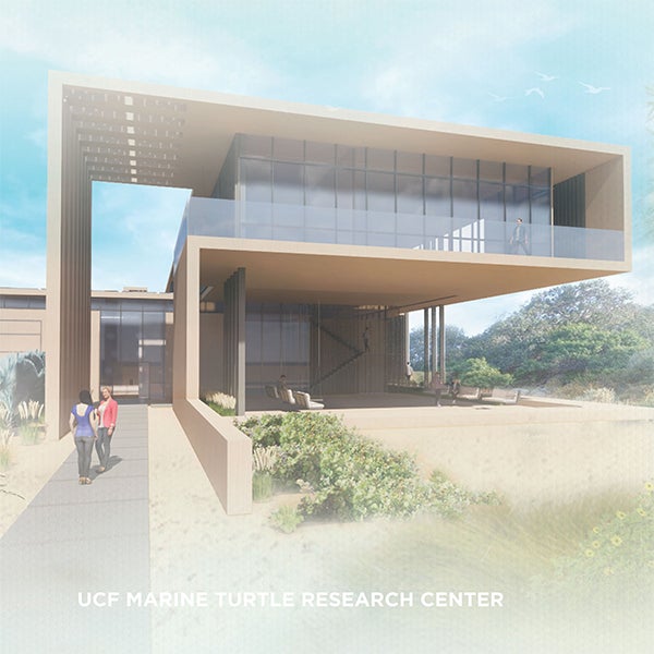 Modern building with large glass windows and elevated structure, labeled "UCF Marine Turtle Research Center," surrounded by sandy landscape and vegetation. Two people walk toward entrance.