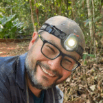 A man with a headlamp and glasses smiling.