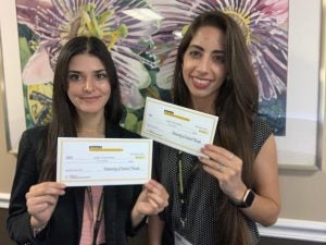 Two women holding "University of Central Florida" checks and smiling while standing in front of a floral art piece.