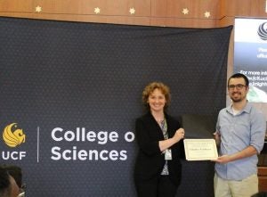 A woman and a man stand in front of a "College of Sciences" backdrop. The woman hands the man a certificate.