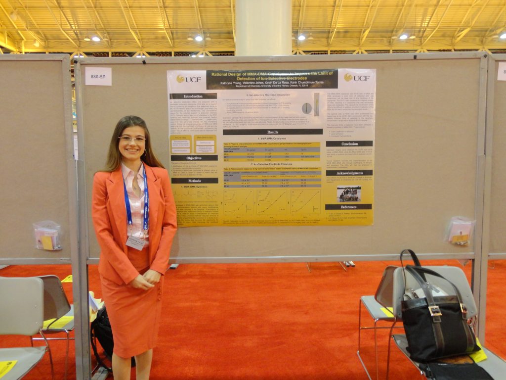 A woman in a business suit standing beside a research poster at a conference.