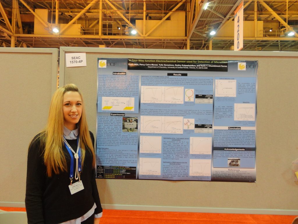 A young woman presenting a scientific poster at a conference or exhibition.