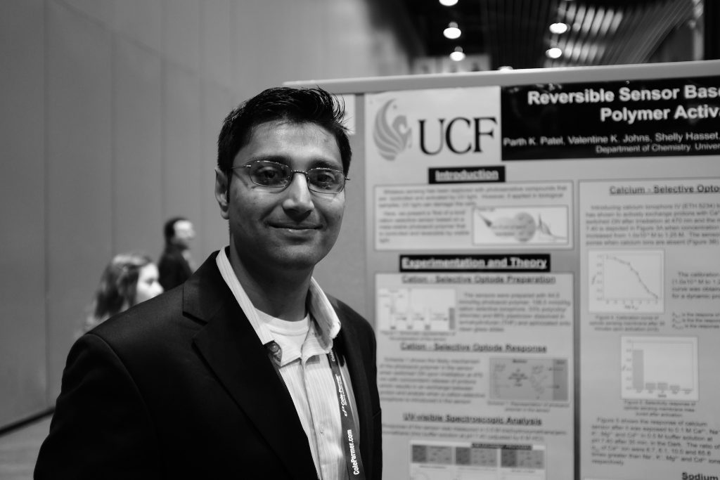 A man in business attire standing in front of a scientific poster presentation.