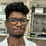 Justin Moore A person wearing glasses and a lab coat is in a chemistry laboratory.