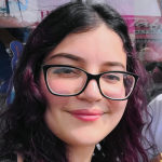 Thais A woman with black-framed glasses and shoulder-length dark hair smiling at the camera.