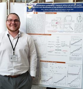 A man stands in front of a scientific poster titled "Low-temperature oxidation of 1-hexanol using a jet-stirred reactor" at a conference. He is wearing a white shirt, tie, and name badge.