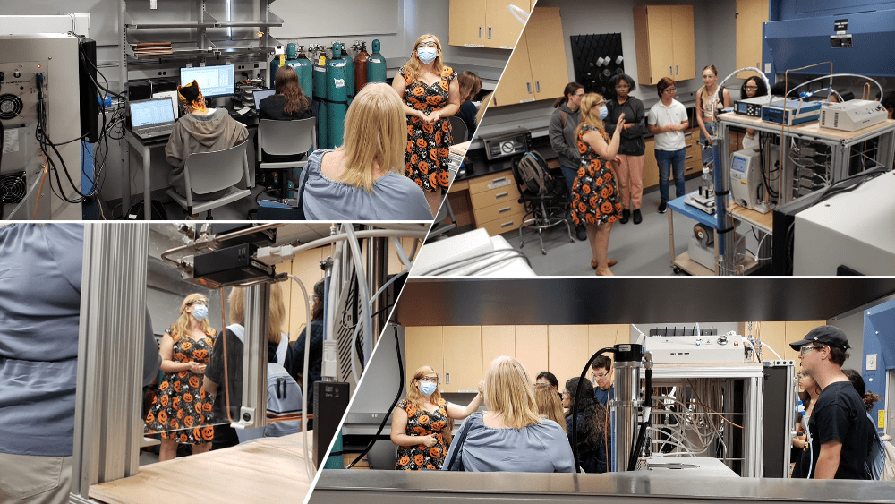 Students are engaged in various laboratory activities, including working on computers, using scientific equipment, and participating in a group discussion led by an instructor in a floral dress.