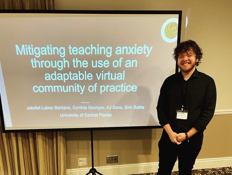 A man standing in front of a presentation about teaching anxiety through the use of a virtual community of practice.