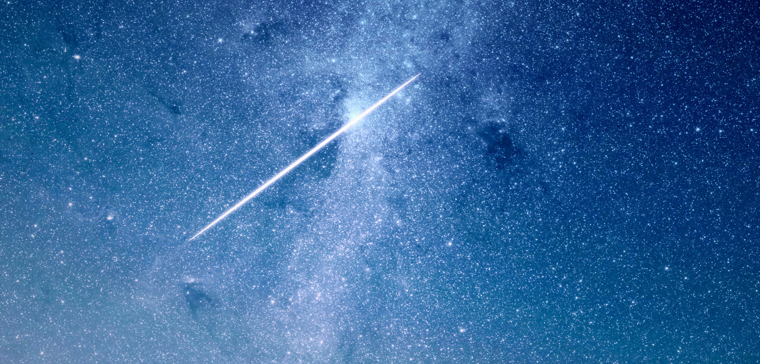 A bright, long meteor streaks across a densely starry night sky, leaving a luminous trail.