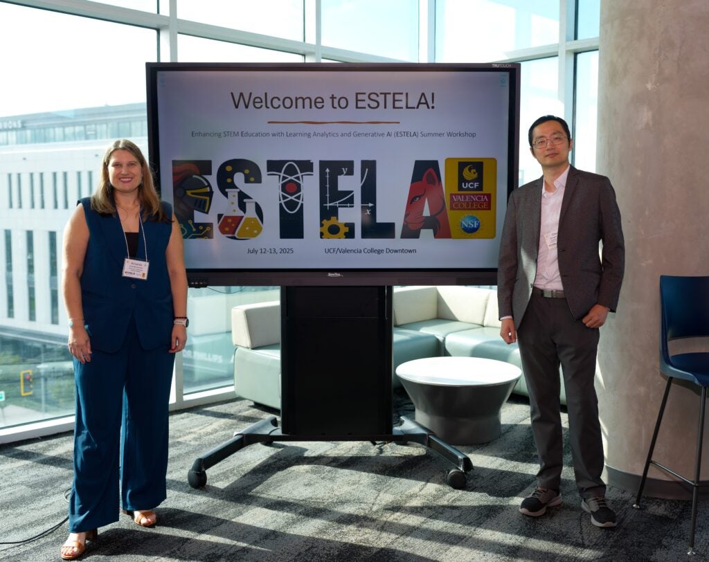 Two people stand beside a large screen displaying the "Welcome to ESTELA!" message at a summer workshop, with university logos and STEM-themed graphics in the background.