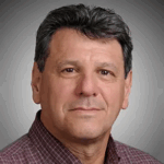 A middle-aged man with short dark hair wearing a maroon checkered shirt, posing in front of a plain gray background.