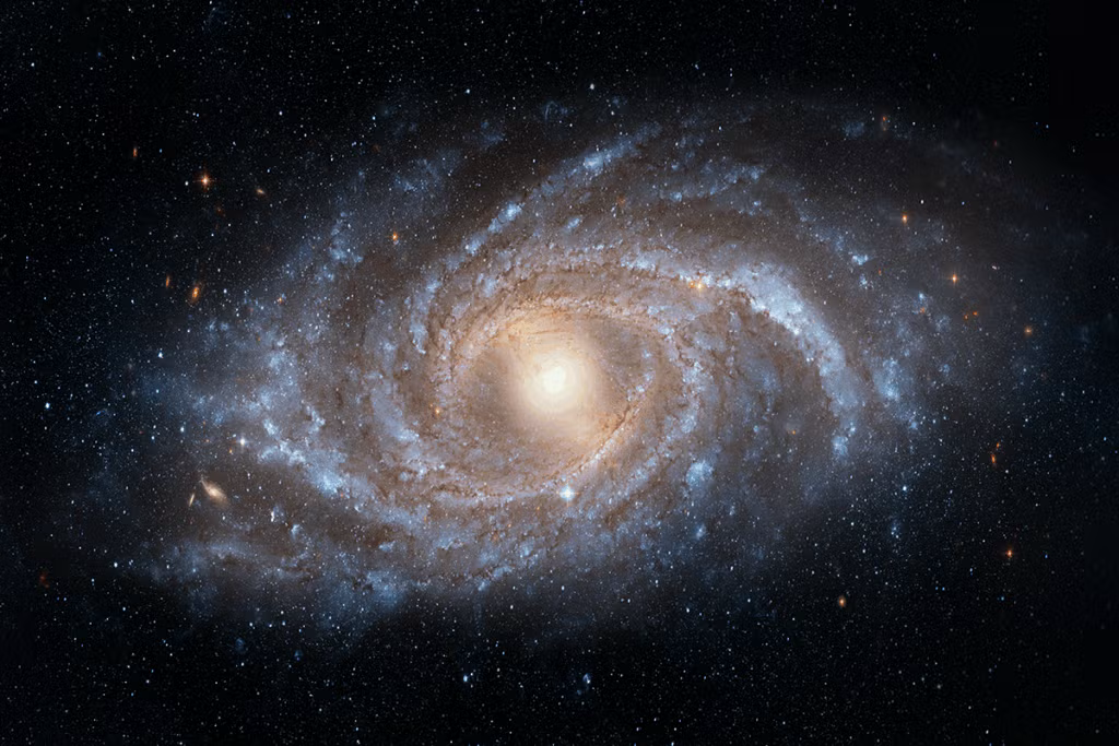 A bright spiral galaxy with a glowing core and sweeping arms filled with stars and dust, set against a background of distant galaxies and deep space.