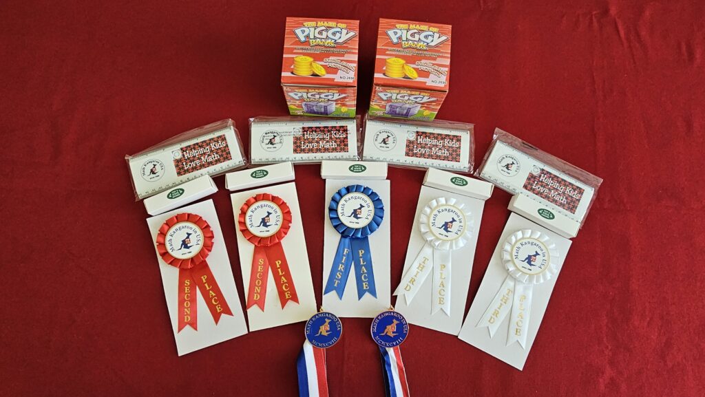 Five award ribbons and medals, two Piggy games, and three clear rectangular boxes are displayed on a red surface.