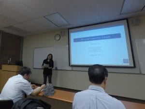 A person presents a lecture on "The Proper Connection of Graphs" with a projected slide in a classroom. Three people are seated in the audience. Date on the slide is March 6, 2017.