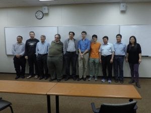 A group of eleven people stands in a classroom in front of a whiteboard, posing for a photograph.