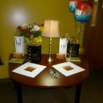 A round table decorated with two gift bags, a bouquet, a balloon, a lamp, and two framed pictures.