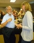 An older man and a middle-aged woman conversing at an office party, surrounded by colleagues.