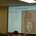 A classroom with students viewing a presentation slide titled "lecture approach" listing several bullet points.