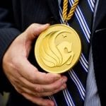 A person in a suit holding a large gold medal with a swan emblem.
