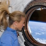 Female astronaut looking out craft window at view of the earth