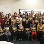 A diverse group of adults proudly displaying certificates in a classroom setting.