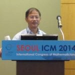 A person presenting at the international congress of mathematics in Seoul, 2014, standing behind a podium with a microphone and a laptop.