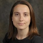 A portrait of a woman with shoulder-length brown hair, wearing a black shirt, set against a gradated brown background.