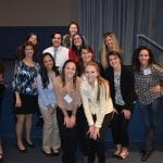 Group of thirteen people posing with smiles in a conference room, some standing in a row while others are kneeling in front.