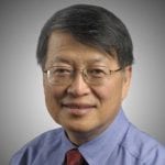 Portrait of a middle-aged asian man wearing glasses, a blue shirt and a red tie, against a gray background.