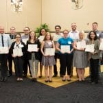 Group of people standing in a conference room, holding certificates, with a 