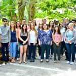 Group of eighteen diverse people standing together in a tropical garden setting.