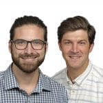 Two smiling men, one with glasses and a beard wearing a plaid shirt, and the other in a striped polo shirt.