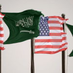 Several flags of the united states and saudi arabia fluttering on poles against a grey sky.
