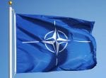A nato flag waving against a clear blue sky, prominently displaying its white compass rose emblem.