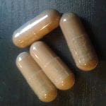 Four brown capsules on a black textured surface.
