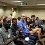 Audience members holding champagne glasses, smiling and conversing in a conference room during an event.