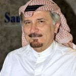 Man in traditional saudi attire with a white thobe and red and white checked keffiyeh, smiling gently at the camera.